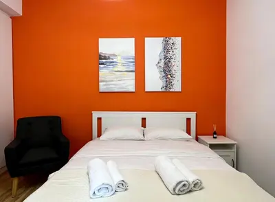 a bedroom with an orange wall with a bed and a black chair at Cozy studio near Flisvos Marina in Athens