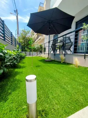 a patio with a table and an umbrella on the grass at Floral Home 1 - ground floor apt, private parking! in Athens