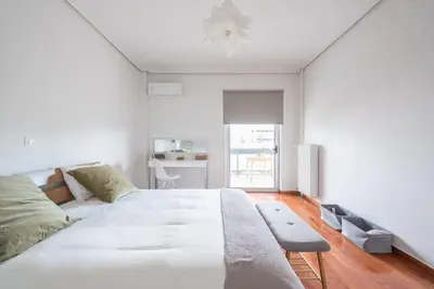 a white bedroom with a large bed and a table at Open -view Apartment, YGEIA Hospital in Athens