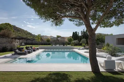 a pool with chairs and a tree in a yard at Villa Vel Aegina in Vaia