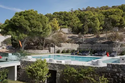 a pool with chairs and umbrellas next to a stone wall at Villa Vel Aegina in Vaia