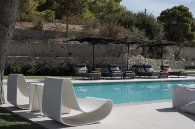 a pool with white chairs and umbrellas next to it at Villa Vel Aegina in Vaia