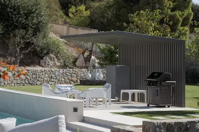 a barbecue grill in a backyard with white chairs at Villa Vel Aegina in Vaia