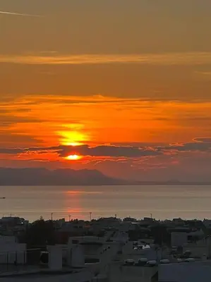 a sunset over the water with a city and the ocean at Luxury Penthouse w/ sea view in Athens