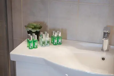 a bathroom sink with green bottles and a vase of flowers at Glyfada Cozy Living in Athens