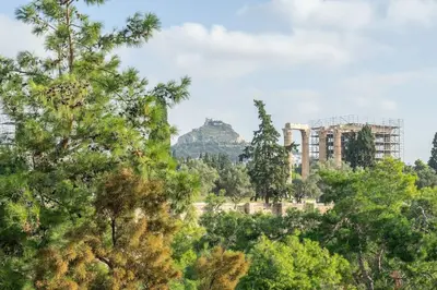 a building in the distance with trees in the foreground at Amazing location - 2 min from Acropolis in Athens