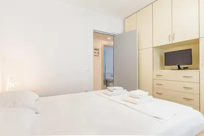 a white bedroom with a large bed and a tv at Elegance Vouliagmeni Gem Luxury Apt, Walk to Beach in Athens