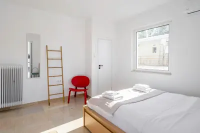 a white bedroom with a bed and a red chair at Voula Panoramic Terraces - Greecing in Athens