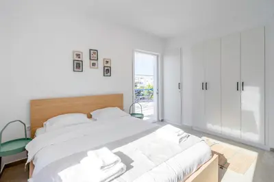 a white bedroom with a bed and a green chair at Voula Panoramic Terraces - Greecing in Athens