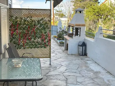 a patio with a table and a hedge with flowers at Peaceful Cottage Porto Rafti in Porto Rafti