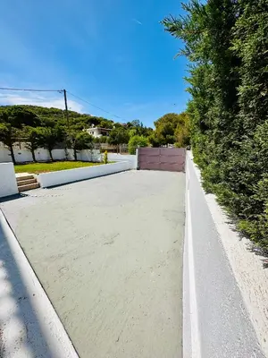 a concrete sidewalk with a fence and trees at Airfenos - Athens Riviera in Anavissos