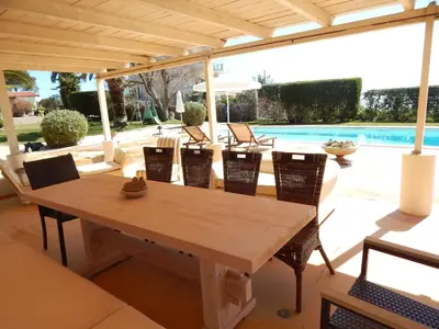 a wooden table and chairs on a patio with a pool at Villa Vravrona Tower & Suites in Markopoulo