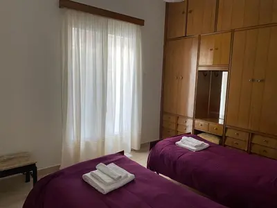 two beds in a room with purple sheets and wooden cabinets at Οικογενειακό Διαμέρισμα στην Αθήνα in Athens