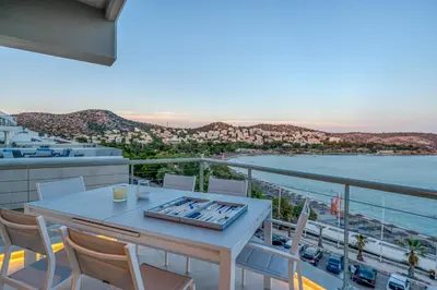 a table and chairs on a balcony with a view of the water at Vouliagmeni - Apollonos Street in Athens