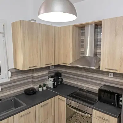a kitchen with wooden cabinets and a large light fixture at Cozy Apartment in Kallithea in Athens