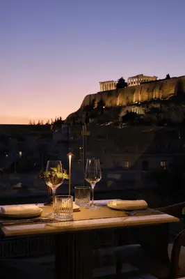a table with wine glasses and a view of the acropolis at Anthology of Athens, The Leading Hotels of the World in Athens