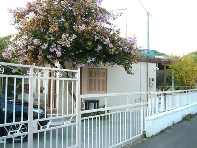 a white fence with a tree with purple flowers at George's Apartment in Agia Marina Aegina