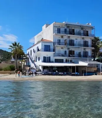 a large white building on the beach with the water at Niko's Beach Suites No1 in Agia Marina Aegina