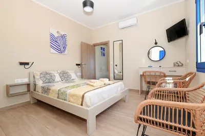 a bedroom with a bed and chairs and a tv at Niko's Beach Suites No1 in Agia Marina Aegina