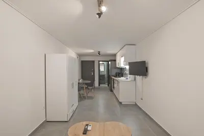 a kitchen and living room with white cabinets and a table at Studio Stratos ideal for 2-3 night Weekends in Athens