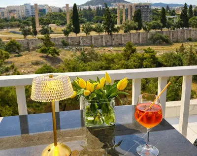 a table with a glass of wine and flowers on a balcony at Acropolis Compass Residence in Athens