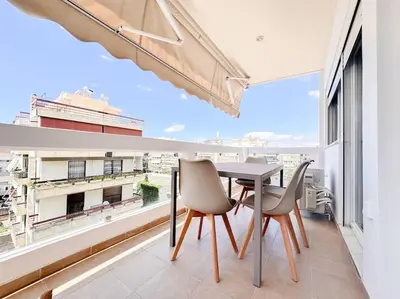 a table and chairs on a balcony with a large window at Pame Rentals - Chic Alimos Home, 5 Min Walk to the Beach in Athens