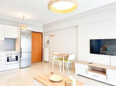 a white kitchen with a table and a refrigerator at Pame Rentals - Chic Alimos Home, 5 Min Walk to the Beach in Athens