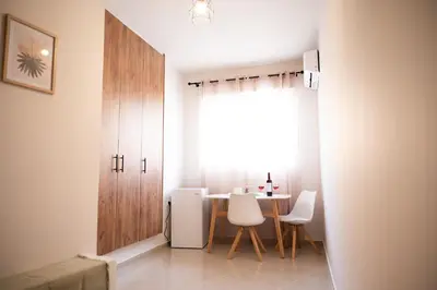 a dining room with a table and white chairs at Anesis Airport Rooms 408 in Koropíon