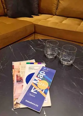 a table with a book and two glasses and a couch at ROYAL BLUE GRAND Suite No 4 Piraeus Port in Piraeus