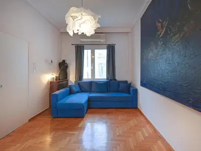 a blue couch in a living room with a painting at Central Pagrati Apartment with Park View Balcony - opp Pangrati Grove in Athens