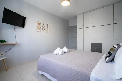 a white bedroom with a bed and a tv at Μercy suit in Piraeus