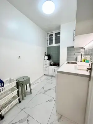 a white kitchen with a counter and a green stool at Cozy appartment Panathianiko Stadio in Athens