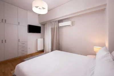 a white bedroom with a white bed and a tv at Acropolis Amazing View: One-Bedroom Gem in Athens