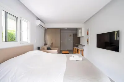 a white bedroom with a large bed and a flat screen tv at Bright & Breezy Glyfada Studio in Athens