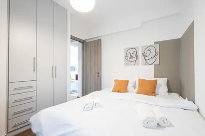a white bedroom with a large bed with orange pillows at Luxury Beachfront Suite in Voula Premium 2-Bedroom Stay in Athens