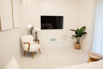 a white living room with a white chair and a tv at J&B Apartment in Athens