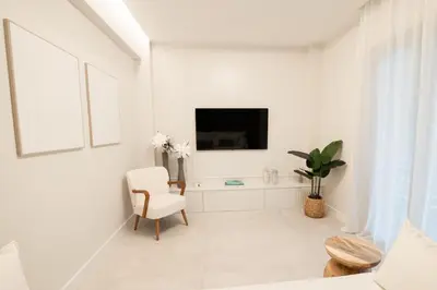 a white living room with a chair and a tv at J&B Apartment in Athens