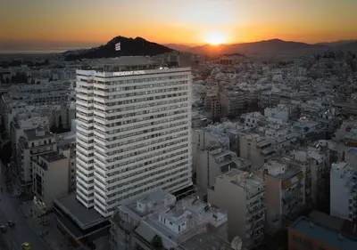 a tall white building with the sunset in the background at President Hotel Athens in Athens