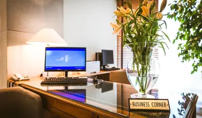 a desk with a computer and a vase of flowers on it at Golden Age Athens Hotel in Athens