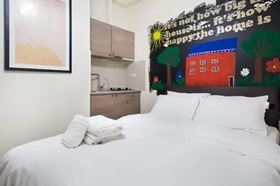a bedroom with a white bed and a kitchen at A comfortable small studio nearby Acropolis 203 in Athens