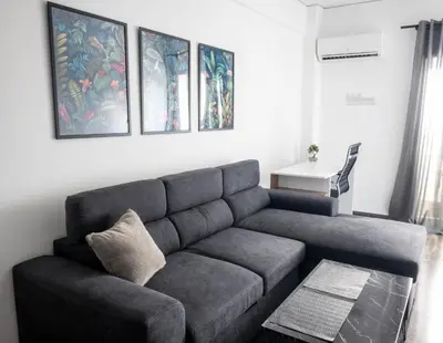 a living room with a gray couch and paintings on the wall at AthensAPTS in Athens