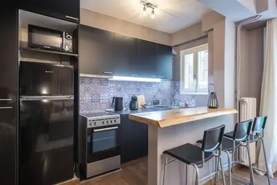 a kitchen with black cabinets and a counter with stools at Athens Seaside Retreat Floisvos in Athens