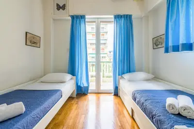 two beds in a room with blue curtains and a window at Spacious Apt Next to Marina Flisvo in Athens