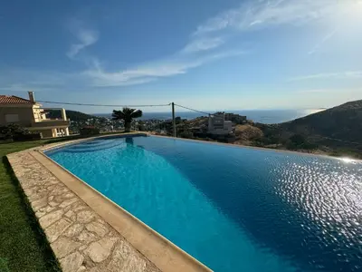 a large blue swimming pool in front of a house at Stone Villa Saronida in Saronida