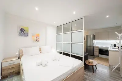 a white bedroom with a large bed and a kitchen at Elegant Athens Downtown Studio in Athens