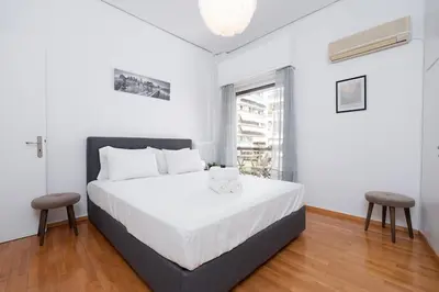 a white bedroom with a bed and two stools at Sea Breeze 2 bedroom Apartment - 10 min walk to beach in Athens
