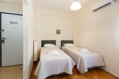 two beds in a room with white walls and wooden floors at Olvios Attiki Metro in Athens