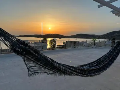 a hammock on a beach with the sunset in the background at Athens Palaia Fokaia Entire Flat 2 bedrooms with panoramic sea views and a massive veranda , only steps away from the beach and amenities in Palaiá Fókaia