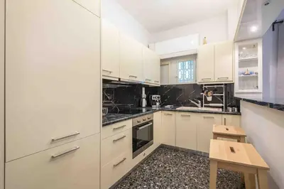 a white kitchen with white cabinets and a wooden stool at Home In The Alimos Marina in Athens