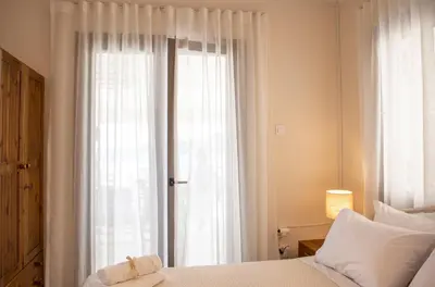a bedroom with a bed and a window with white curtains at Sea La Vie in Agia Marina Aegina